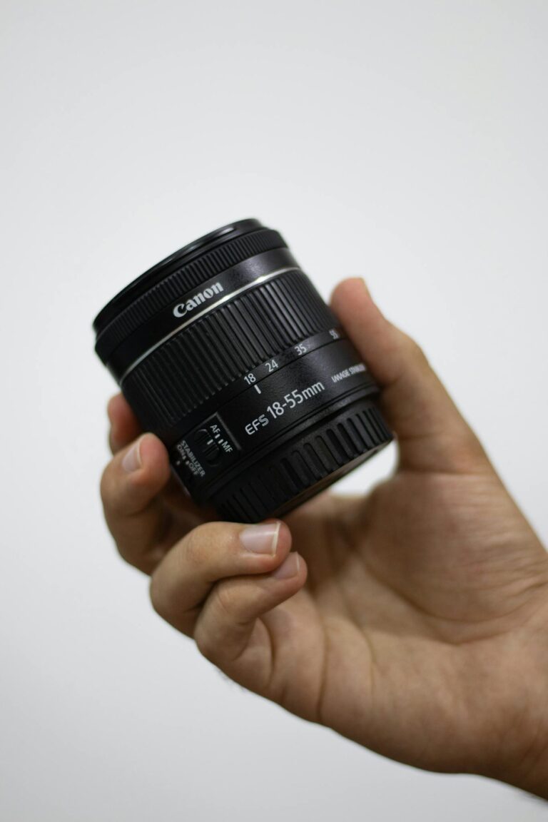 Detailed image of a hand holding a Canon camera lens indoors.